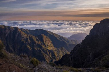 Pico do Arieiro 'nun görkemli zirveleri, güneş ışığının engebeli manzarayı aydınlattığı Madeira' da gün batımında aşağıdaki bulutlarla çarpıcı bir tezat oluşturduğu gibi görülebilir..