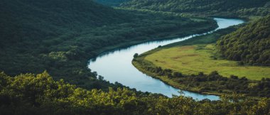 Güneş ışığı, yemyeşil bir vadide kıvrılan sakin bir nehri nazikçe aydınlatır..