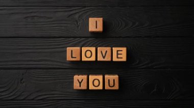 Stop-motion wooden cubes with the phrase I Love You on a black background - a wooden table. Words of love are made of letters from wood for your girlfriend, boyfriend, wife, husband, for Valentines