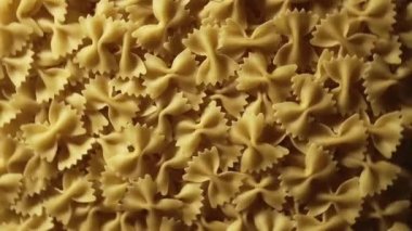 Uncooked Farfalle pasta rotating in fast motion - top view, flat lay, low key, food background. Raw dried organic golden macaroni texture. Italian food, cuisine and culture close up. Classic dry