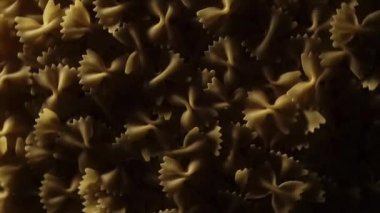 Hızlı çekimde dönen pişmemiş Farfalle makarnası. Üst görüş, düz konum, sade anahtar, yemek arka planı. Çiğ organik altın makarna dokusu. İtalyan yemeği, mutfağı ve kültürü yakından takip edin. Klasik kuru.