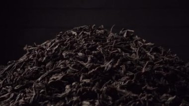 Bir yığın siyah yaprak çayı koyu siyah arka planda yavaşça döner. Yakın plan, kenar görünüm