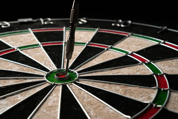 One dart hits the bulls eye of a dartboard on a black wooden background. Happy win and luck concept. Close-up, angled view