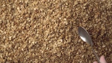 Arka planda bir yığın yulaf ezmesi ya da çıtır çıtır ve elinde bir kaşık, kepçeleme ve inceleme. Sağlıklı gıda kavramı - mısır gevreği kahvaltısı. Yaklaş, üstten bak. Reklam metni için alanı kopyala