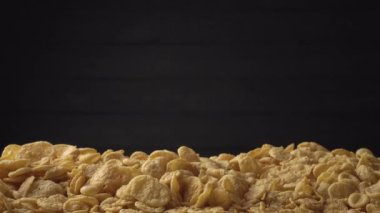 Bir yığın sarı mısır gevreği siyah arka planda bir yığın üzerine düşüyor. Sağlıklı gıda kavramı - mısır gevreği kahvaltısı. Yakın plan, yan görüş. Reklam metni için alanı kopyala