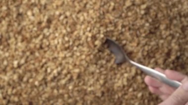 Arka planda bir yığın yulaf ezmesi ya da çıtır çıtır ve elinde bir kaşık, kepçeleme ve inceleme. Sağlıklı gıda kavramı - mısır gevreği kahvaltısı. Yaklaş, üstten bak. Reklam metni için alanı kopyala