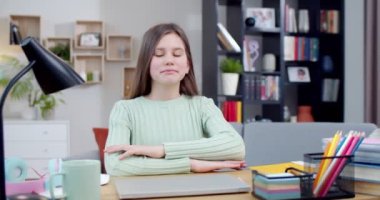 Oturma odasında masasında oturan ve kameraya gülümseyen beyaz bir genç kızın portresi. İçeride. Evde ödev yaparken güzel bir liseli kız. Zeki genç kız..