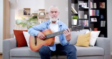Oturma odasında kanepede otururken gitar çalan beyaz saçlı son sınıf öğrencisi. Yaşlı bir erkek emekli evde müzik çalıyor. Koltukta müzik aleti olan bir büyükbaba. İçeride..