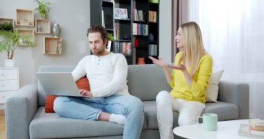 Yakışıklı beyaz adam kanepede oturup dizüstü bilgisayarda çalışırken genç ve güzel karısı onu rahatsız edip rahatsız ediyor. Küçük kadın konuşuyor ve meşgul kocasını rahatsız ediyor. Ev ödevi.