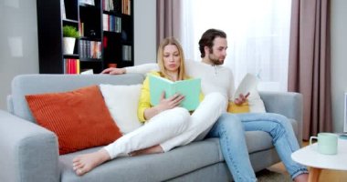 Kafkasyalı genç bir çift, rahat bir oturma odasında kanepede oturup birbirlerine ilginç kitaplar okuyup sarılıyorlar. - Evde. Kapalı alanda. Güzel kadın ve yakışıklı adam edebiyatta hikayeler okurlar..