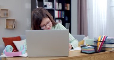 Gözlüklü oldukça zeki bir öğrenci dizüstü bilgisayarda oturuyor, evde yazma egzersizi yapıyor ve çevrimiçi ders veriyor. İnternetten öğrenim görüyor. Genç kız evde bilgisayar öğreniyor, ödevini yazıyor. Eğitim kavramı.