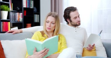 Ciddi bir beyaz kadın ve erkek olan evli çiftin evde vakit geçirip kitap okuduğu yakın plan. İçeride. Koltukta ders kitapları olan erkek ve kadın okurlar..