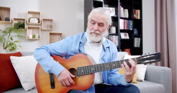 Caucasiano Velho Homem Cabelos Grisalhos Tocando Guitarra Enquanto Sentado Sofá — Vídeo de Stock