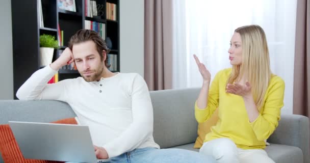 若い白人ハンサムな男は ラップトップコンピュータで働いて かなり女性が彼と迷惑な話をしながら集中しようとしています 妻と夫は気分の概念で区切られた — ストック動画