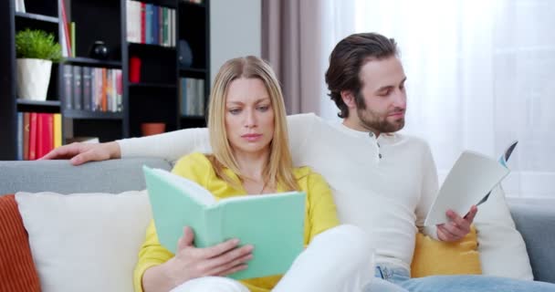 幸せな笑顔白人の女性と男性 結婚したカップルは家で一緒に余暇を過ごし 面白い本を読んでいます 屋内だ ソファに腰かけながら笑っている男女の読者 喜劇書 — ストック動画