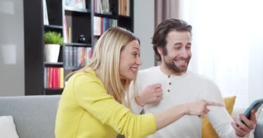 Mutlu erkek ve kadın, oturma odasındaki koltukta oturan evli çift cep telefonundan bir şey kazanmış ya da harika sonuçlar almış gibi neşeleniyorlar. Erkek ve kadın gülüyor ve zaferi kutluyor..