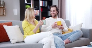 Neşeli, genç, beyaz bir erkek ve kadın evde oturup konuşuyor, gülümsüyor ve kahve ya da çay içiyor. Evli çift sıcak içkileri yudumluyor ve düşüncelerini paylaşıyorlar. Kapalı.