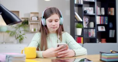 Beyaz tenli güzel, kulaklıklı, akıllı telefonuyla oynayan ve evde müzik dinleyen bir kız. Güzel, mutlu bir çocuk cep telefonuyla sohbet ediyor. Gülümsüyor ve şarkıdan keyif alıyor. İçeride..
