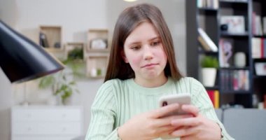 Kafkasyalı şirin kız rahat bir oturma odasında masada otururken cep telefonuyla mesajlaşıp sohbet ediyor. İçeride. Güzel, mutlu, gülümseyen liseli kız akıllı telefondan mesaj yolluyor..