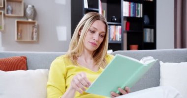Kanepede kitap okuyan güzel bir bayan ilgini çekti. Güzel bir kadın kitabın sayfasını çeviriyor ve rahat bir odada gülümsüyor. Kullanışlı eğlence, aktivite, boş zaman. Okuma konsepti.