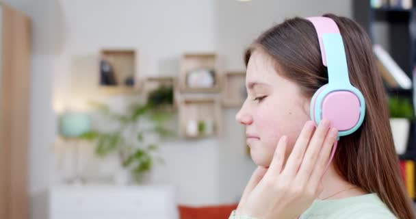 在舒适的客厅里 坐在耳机里听音乐的白人小女孩的近视 年轻美丽的女学生喜欢唱歌 在家里侧视图 — 图库视频影像