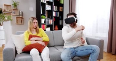 Sanal gerçeklik oyununda dans eden neşeli adam kanepesinde güzel bir kadınla müzik dinliyor. Evde şaşkın bir kadınla VR gözlükleriyle oynayan neşeli, rahatlatıcı bir erkek. VR oyun konsepti.