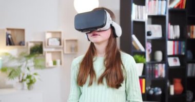 Geniş oturma odasında VR gözlükleri takmış oyun oynayan yakın plan genç kız. Genç liseli kız el ele hareket ediyor, jestler yapıyor, video oyununda hareket etmek için joystick 'i tutuyor. VR kavramı.