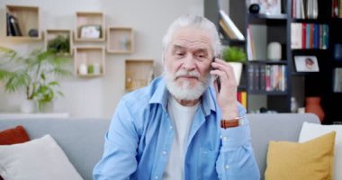 Şık, çekici, yaşlı bir adam telefonda konuşuyor. Güzel beyefendi evdeki kanepede oturup iletişim kurmak için akıllı telefonu kullanıyor. Gri sakallı ve saçlı yaşlı bir adam. İletişim konsepti.