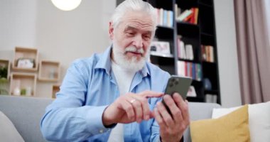 Yakından bakınca yakışıklı büyükbaba oturma odasında telefon kullanıyor. Koltuğunda telefonu tutan, tıklayan, kaydıran yaşlı adam. Son sınıf öğrencisi, iPhone 'lu kot pantolon giyiyor. Teknoloji konsepti.