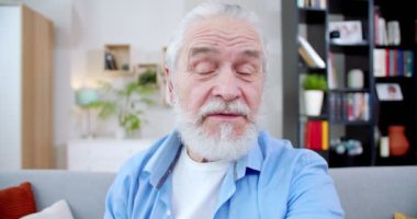 Yakışıklı, yaşlı bir adam renkli bir odada oturuyor. Yaşlı, yakışıklı, gri saçlı, ailesi için video çağrısı yapan bir erkek. Mutlu son sınıf öğrencileri el hareketleri yapıyor, insanlarla konuşuyor. Video çağrısı kavramı.