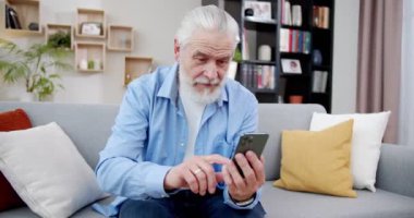 Yakın plan yaşlı adam elinde, koltukta otururken telefon kullanıyor. Yaşlılar akıllı telefon öğrenme tuşuna basmakla meşgul. Son sınıf öğrencisi, iPhone 'lu kot pantolon giyiyor. Teknoloji konsepti.