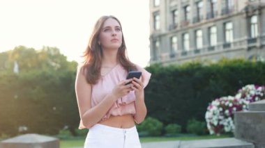 Kasabada yürürken akıllı telefondan mesaj atan neşeli beyaz bir genç kadın. Dışarıda cep telefonuyla yazarken gülümseyen güzel bir kız. Şehir konsepti