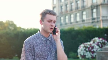 Genç beyaz bir adam şehirde yürüyor ve akıllı telefondan konuşuyor. Neşeli beyaz erkek sokakta yürürken akıllı telefon kullanıyor..