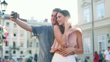 Birbirine aşık genç bir çift sokakta durup fotoğraf, selfie, fotoğraf çekiyor. İnsanlar video çekmek için akıllı telefon kullanıyor, dışarıda kameraya poz veriyorlar. Fotoğraf, teknoloji, alet.