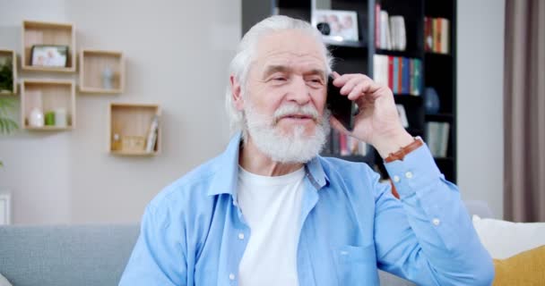クローズアップ電話で話して灰色の髪とひげをリラックスした老人 スマートフォンで人を呼ぶ上品なシニア男性 見事な高齢者のスタイリッシュな服を着て 見てください 電話のコンセプト — ストック動画