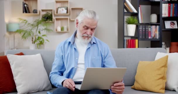 Γέρος Χρησιμοποιεί Λάπτοπ Καθισμένος Στον Καναπέ Προσοχή Ηλικιωμένοι Αναζητούν Ανάγνωση — Αρχείο Βίντεο