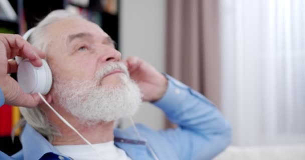 Atrakcyjny Staruszek Słuchający Muzyki Siedzącej Kanapie Radosny Starzec Cieszący Się — Wideo stockowe