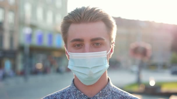 接近年轻的高加索人 脸上戴着医疗面具 看着相机 城里站在街上的漂亮男人 — 图库视频影像