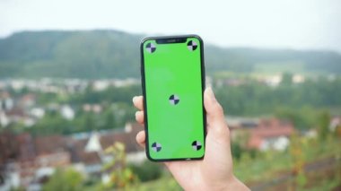 Atletik kadın yeşil ekranı akıllı telefonuyla kullanıyor ve sokakta dikiliyor. Açık hava egzersizlerinden sonra sosyal medyada kadın paylaşımına uygun.