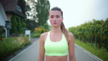 Şehir caddesinde duran başarılı kadın sporcu kıyafeti şampiyonu. Yetişkin beyaz bir kadın ciddi bir suratla kameraya bakıyor. Spor, eğitim, sağlıklı ve sağlıklı bir yaşam tarzı.