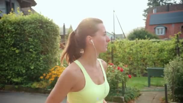 若い白人女性が屋外でイヤホンをつけて走り 音楽を聴いています 健康的なランニングと屋外運動の概念 — ストック動画