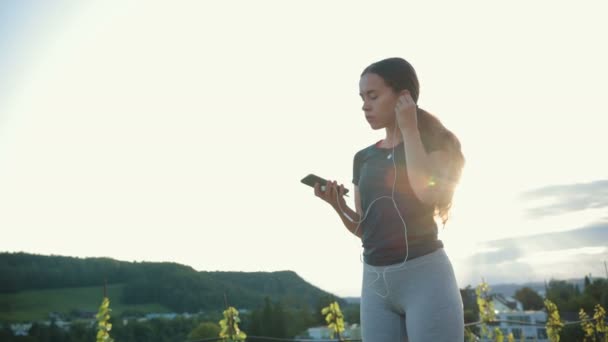 若い白人女性はイヤホンをつけて音楽を聴き 屋外で走り始めた 健康的なランニングと屋外運動の概念 — ストック動画
