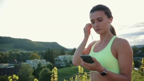 年轻的高加索女性戴着耳机 听着音乐 开始在户外跑步 健康跑步及户外运动的概念 — 图库视频影像