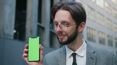 Yakışıklı, gülümseyen beyaz adamın portre fotoğrafı yeşil ekran ve takip hareketleriyle akıllı telefon gösterisi yapıyor. Krom anahtar kavramı