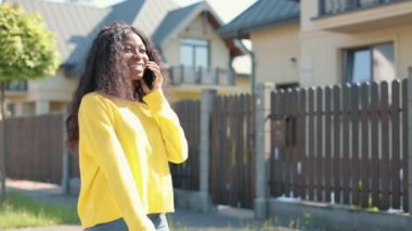 Şık, çok kültürlü, neşeli, caddede yürüyen ve akıllı telefonun başında neşeli, dişlek gülüşlü biriyle konuşan kıza yakın durun. Kadın konsepti portresi