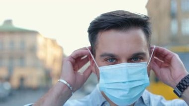 Caddede dikilip kameraya bakan çekici erkek portresi. Dışarıda tıbbi koruyucu maske takan genç beyaz bir adam. Virüs, covid-19, sağlık, güvenlik kavramı