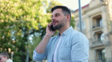 Caddede dikilen neşeli beyaz adamın portresi. Cep telefonuyla arayıp konuşurken gülümsüyor. Akıllı telefondan sohbet ederken kahve içen mutlu yakışıklı erkek. Şehir konsepti