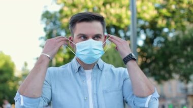 Yüzüne tıbbi maske takan ve kameraya bakan beyaz bir genç. Kasabada caddede duran güzel bir erkek