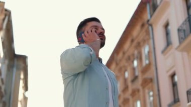 Genç beyaz bir adam şehirde yürüyor ve akıllı telefondan konuşuyor. Neşeli beyaz erkek sokakta yürürken akıllı telefon kullanıyor.