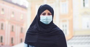 Çekici peçeli kadın müslüman sokakta dikilip kameraya bakıyor. Tıbbi koruyucu maskeli yetişkin bir Arap kadın açık havada tesettür takıyor. Din, insanlar, kültür kavramı.